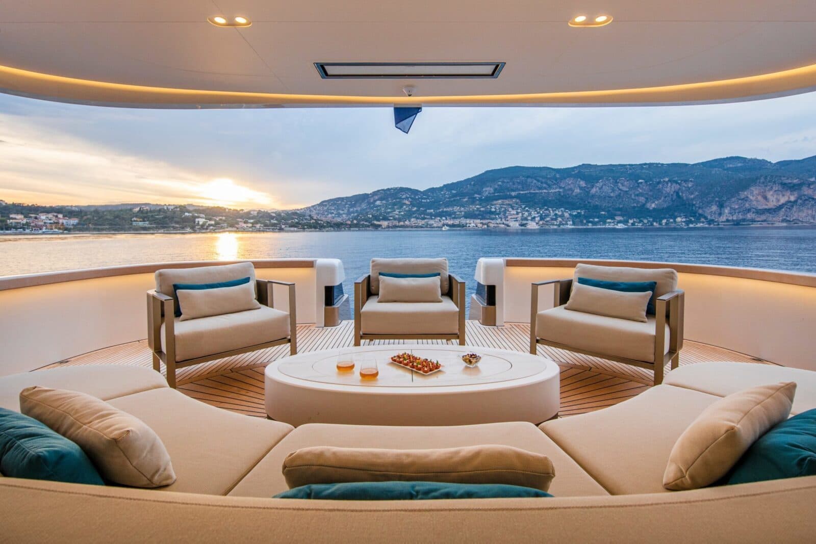 Outdoor lounge seating on a sunlit deck overlooking the sea at dusk.