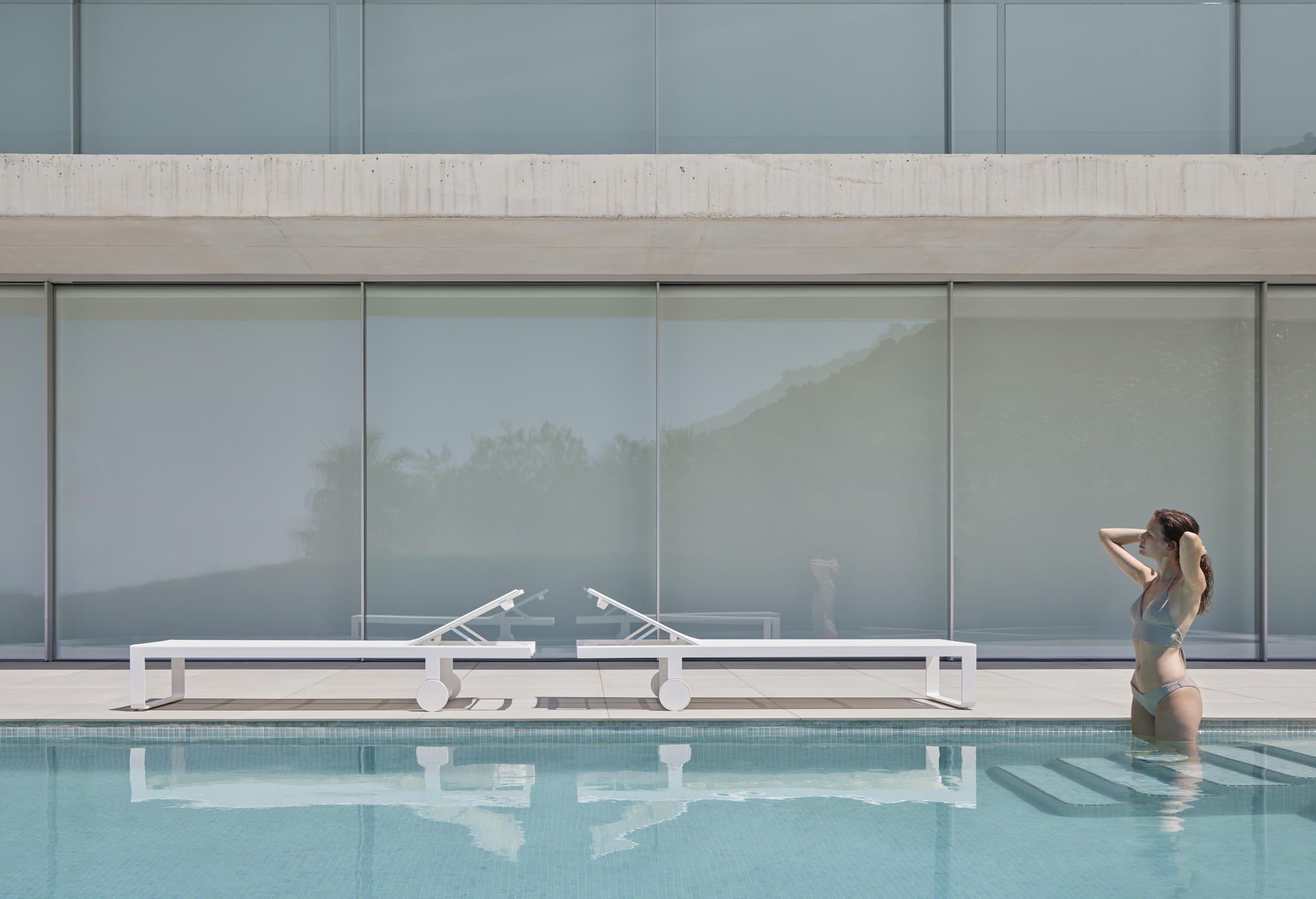Flat Textil high chaise lounges at a glass-walled pool.
