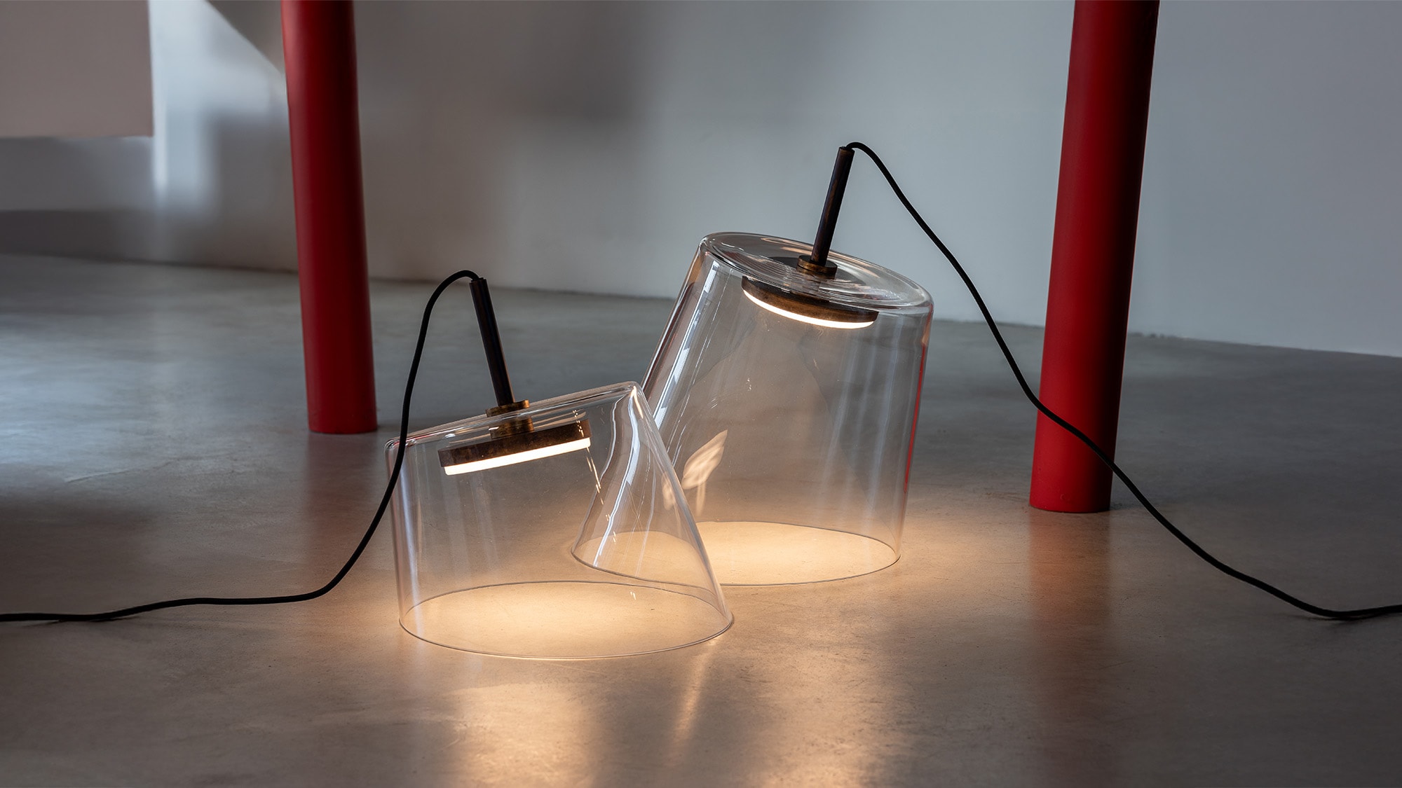 Hind Rabii hand-blown glass pendant lights glowing on a concrete floor.