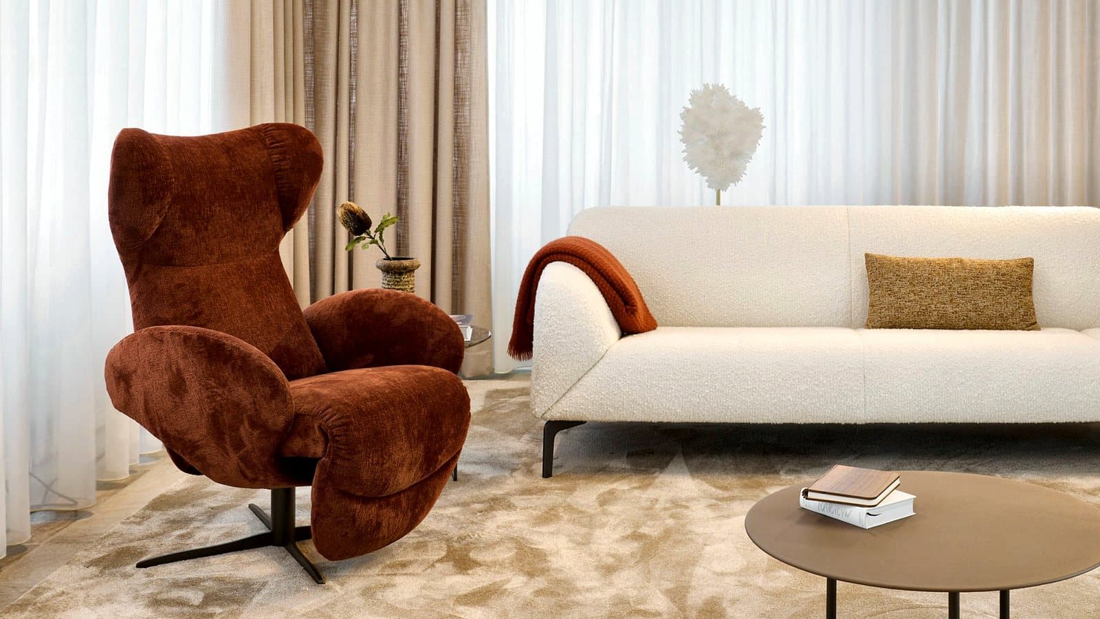 A rust-toned lounge chair and bouclé sofa in a calm, light-filled interior.